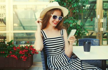 Güzel genç bir kadın bir kafede telefonuyla oturuyor.