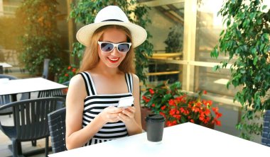 Güzel genç bir kadın bir kafede telefonuyla oturuyor.