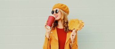 Sarı akçaağaç yaprakları ve gri arka planda Fransız beresi takan gülümseyen kadının sonbahar portresi.