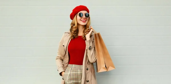 ショッピングバッグと笑顔の女性の秋の肖像離れてコートを着て グレーの背景に赤いフランス語ベレー帽 — ストック写真