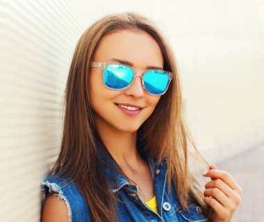 Şehirde mavi güneş gözlüğü takan çekici genç bir kadının yaz portresini kapat.