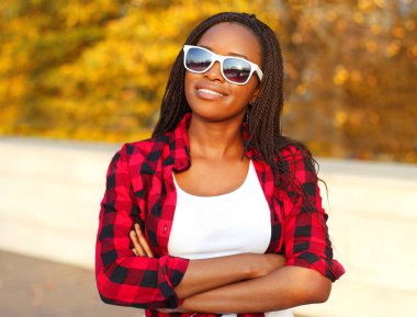Sonbahar günü güneş gözlüğü takan gülümseyen Afrikalı genç bir kadının portresi.