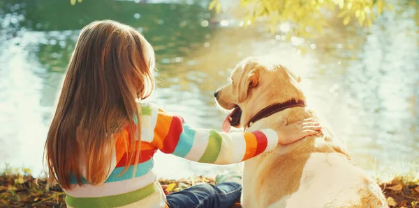 小さな女の子子供とともにLabraador取得犬座っている晴れた夏の公園近くの川 — ストック写真