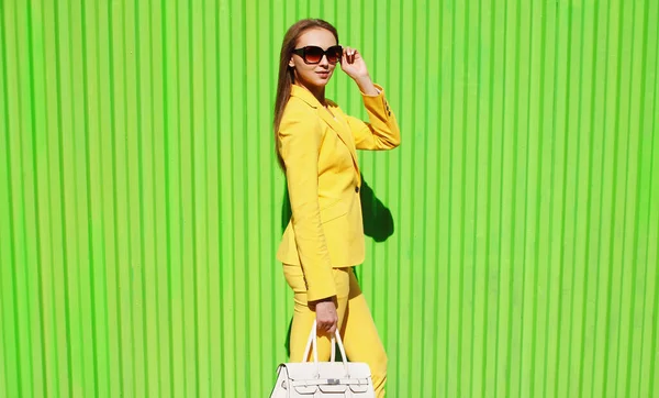 美しい女性です黄色のスーツにバッグで街の緑の背景 — ストック写真