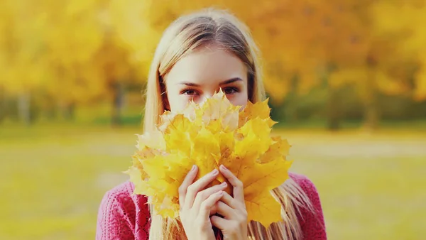 秋の公園で黄色のカエデの葉を持つ美しい笑顔ブロンドの女性の肖像画 — ストック写真