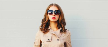 Şehirde ceketli, güneş gözlüklü, gri arka planda çekici bir kadın portresi.