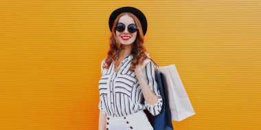 Portakal rengi arka planda siyah yuvarlak şapkalı ve çizgili beyaz gömlekli çekici bir kadın portresi.