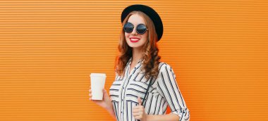 Siyah yuvarlak şapkalı, turuncu arka planda çizgili beyaz gömlekli, kahve fincanı olan çekici bir kadının portresi.