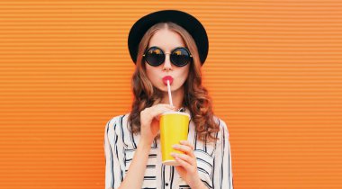 Portakal suyu ya da kahve içen çekici bir kadının portresi turuncu arka planda siyah yuvarlak bir şapka takıyor.
