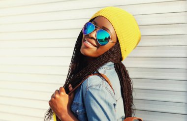 Şehrin arka planında güneş gözlüğü takan mutlu, gülümseyen Afrikalı bir kadının portresi.