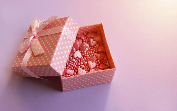 Gift open pink box with topping from hearts inside.