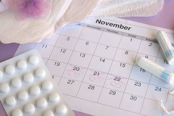 Menstrual pads and tampons on menstruation period calendar with on lilac background.