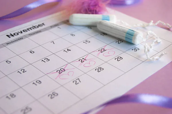 Menstrual pads and tampons on menstruation period calendar with on lilac background.