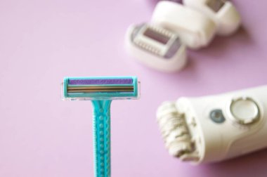 Epilatörün arka planında izole edilmiş tek kullanımlık tıraş makinesinin seçici odaklı yakın görüntüsü. Tıraş bıçağı ve cilt bakımı konseptiyle kadın ve erkek tüy dökümü tedavisi. Epilasyon tüy dökücü..