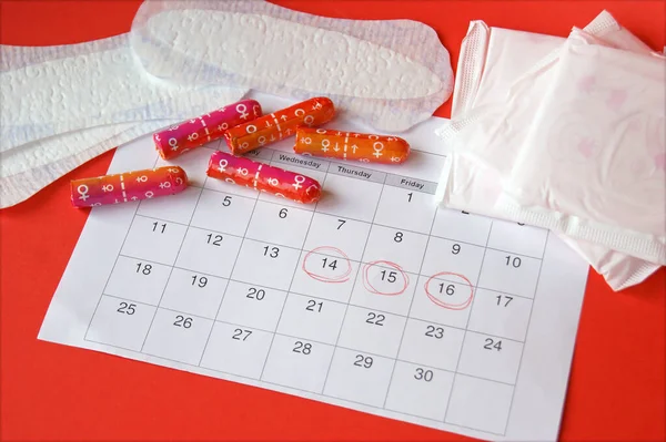 背景が赤の月経期間カレンダー上の月経パッドとタンポン — ストック写真