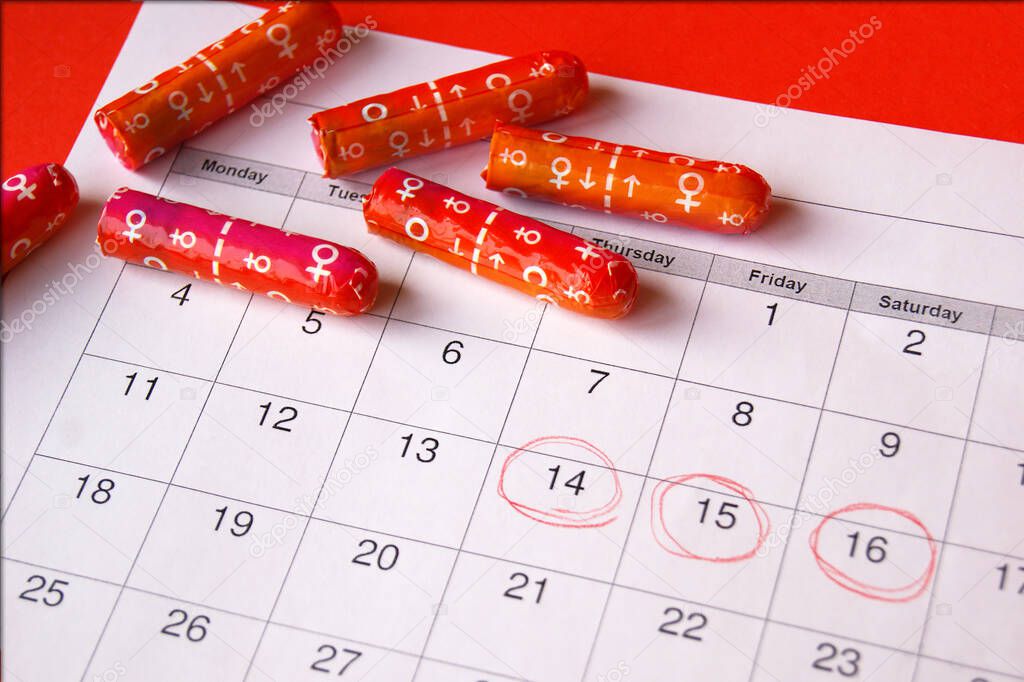 Menstrual pads and tampons on menstruation period calendar with on red background.