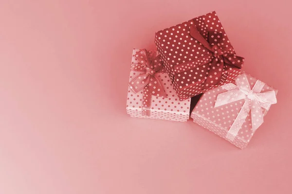 Wrapped Christmas or other holiday handmade present in paper with pink ribbon on coral background. Present box, decoration of gift on colored table, top view with copy space