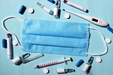 Üç katmanlı bir tıbbi maske, lastik kulak bantları, bir şırınga, bir termometre ve çeşitli ilaçlar, tabletler, aşılar. Tıp konsepti, zamanında aşı ve sağlık.