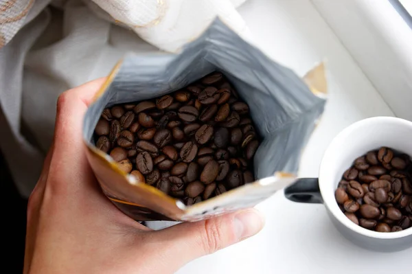 Mano Tiene Pacchetto Aperto Chicchi Caffè Sullo Sfondo Una Tazza — Foto Stock