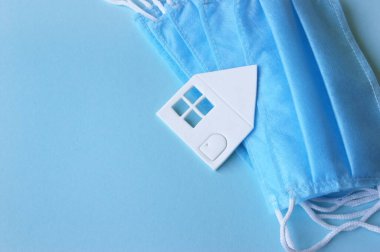 Üç katmanlı, plastik kulaklıklı bir tıbbi maske, beyaz kağıt ev. Tıp konsepti. Umut. Evde kal, güvende kal..