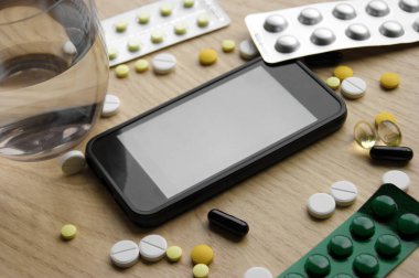 Düz konuma yakın elektronik termometre ve ilaç rengi beyaz, turuncu, sarı ve siyah haplar. Yukarıdan çekilmiş ve seçici bir odak noktası var. Üst görünüm