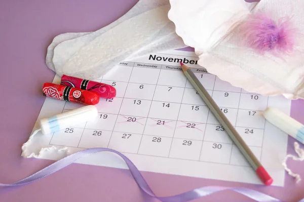 Menstrual pads and tampons on menstruation period calendar with on lilac background.