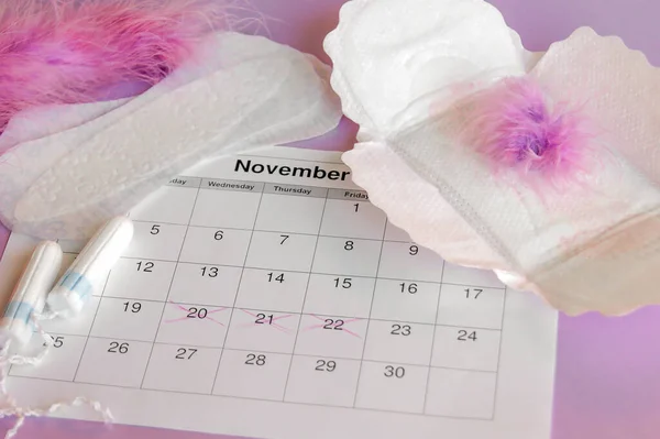 Menstrual pads and tampons on menstruation period calendar with on lilac background.