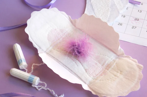 Menstrual pads and tampons on menstruation period calendar with on lilac background.