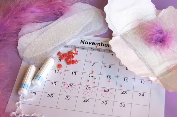 Menstrual pads and tampons on menstruation period calendar with on lilac background.