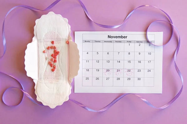 Menstrual pads and tampons on menstruation period calendar with on lilac background.