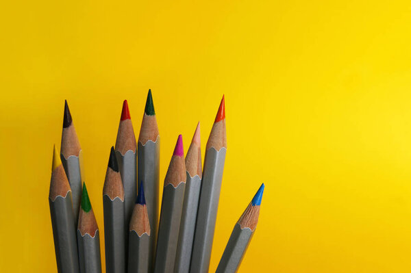 Many colorful pencils laying on a beautiful yellow background. There is a copy space.