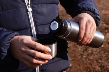 Adamın elleri termostan fincana taze sıcak kakao döküyor. Gezmek ve sonbahar ya da bahar doğa kavramının fotoğraflarını çekmek.