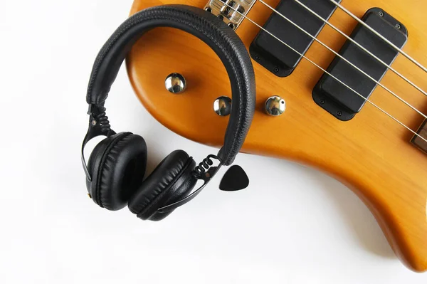 Portable black headphones and bass guitar on white background. Layout, creative design, bright frame with text space.Music lifestyle. Youth earphones.