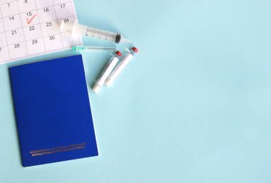 Mavi Uluslararası veteriner pasaportu, şırınga ve açık mavi arka planda sıvı bulunan ampul. Takvimde işaretli tarih, evcil hayvanlar için yıllık aşı kavramı. Üst Manzara. Metin için alanı kopyala.