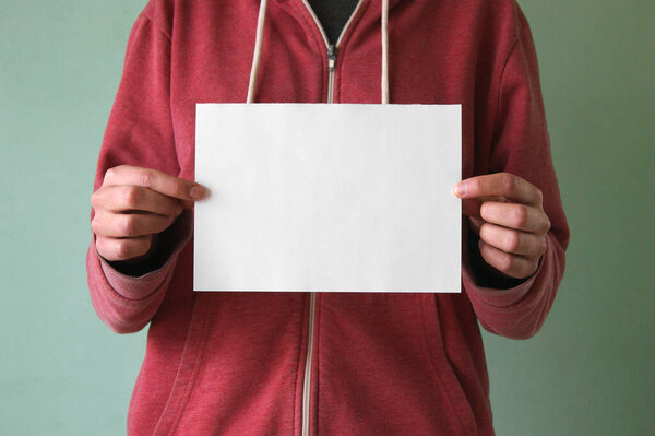 A young man holds an empty sheet of paper. Place for text.