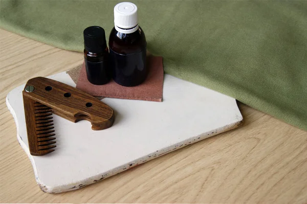 Male wooden comb for beard and hair, care oils on white desk. Compact folding comb that you can always take with you. Beard and hair care concept.