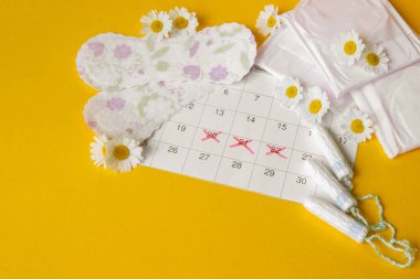 Adet takviminde regl pedi ve tampon. Sarı arka planda papatyalar. Kadın sağlığı kavramı, kritik günlerde kişisel hijyen.