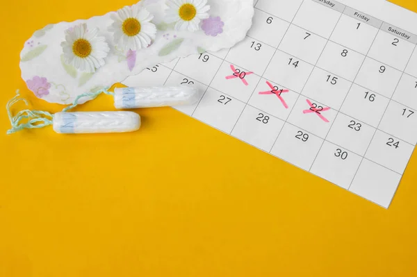 Menstrual pads with chamomiles on menstruation period calendar on yellow background. The concept of female health, personal hygiene during critical days.
