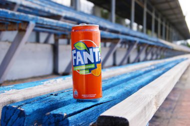 KHARKOV, UKRAINE - 12 Haziran 2020: Küçük bir stadyumdaki ahşap bir bankta duran metal bir Fanta içeceği şişesi. Bulanık arkaplan.