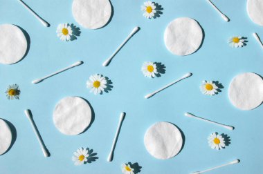 Kulak çubukları, beyaz pamuk pedler ve mavi arka planda papatyalar. Vücut hijyeni ve kişisel bakım kavramını.