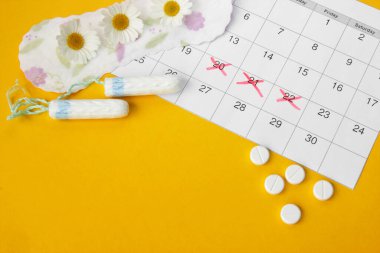 Adet takviminde regl pedi ve tampon. Sarı arka planda papatyalar. Kadın sağlığı kavramı, kritik günlerde kişisel hijyen.