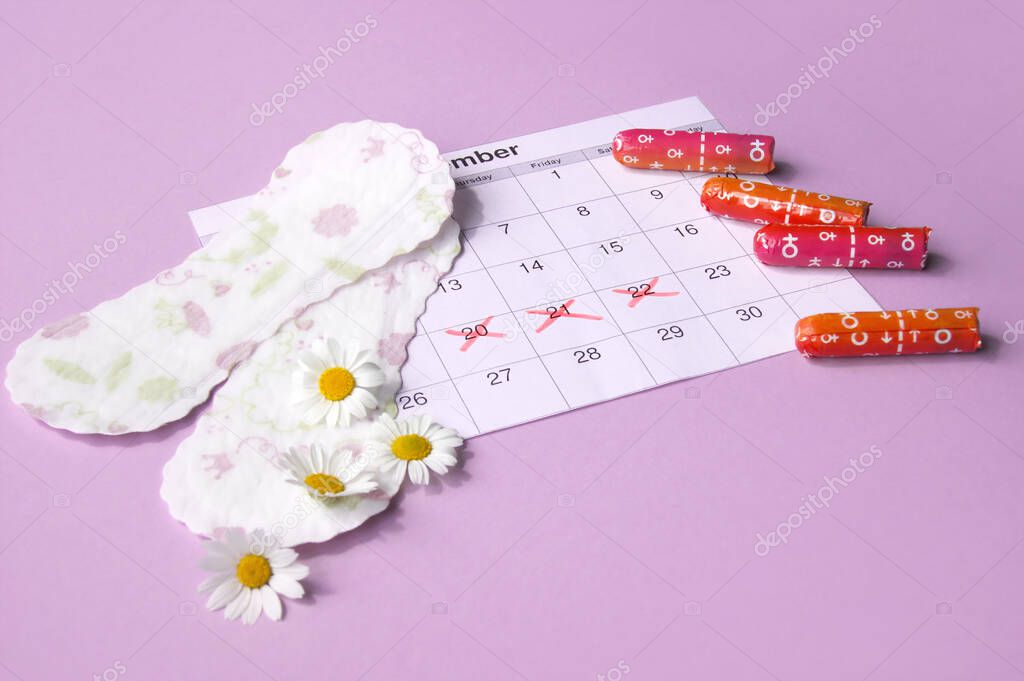 Menstrual pads and tampons on menstruation period calendar with chamomiles on pink background. The concept of female health, personal hygiene during critical days.