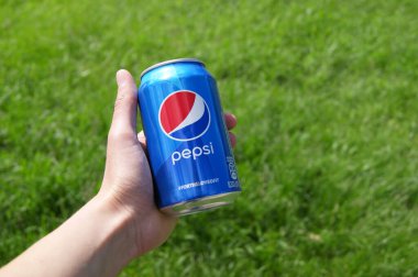 KHARKOV, UKRAINE - 12 Haziran 2020: El, yeşil çimenlerin arka planında Pepsi 'nin metal kutusunu tutuyor.