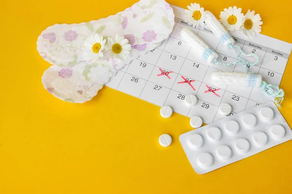 Menstrual pads and tampons on menstruation period calendar with chamomiles on yellow background. The concept of female health, personal hygiene during critical days.