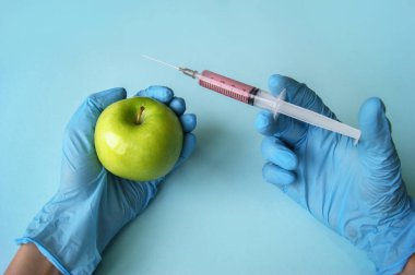 Mavi arka planda GDO 'lu yeşil elma ve şırınga. Sebze ve meyvelerle GDO kavramı.