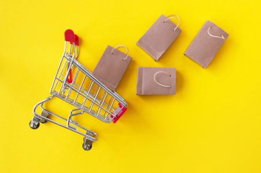 Sarı arka planda küçük el çantaları olan mini alışveriş arabası. Üst Manzara. Mağazalarda ve internette alışveriş kavramı.