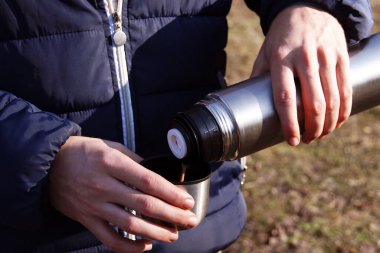 Adamın elleri termostan fincana taze sıcak kakao döküyor. Gezmek ve sonbahar ya da bahar doğa kavramının fotoğraflarını çekmek.