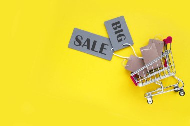 Küçük el çantalı mini alışveriş arabası ve sarı arka planda büyük indirim yazılı gri etiketli. Mağazalarda ve internette alışveriş kavramı.
