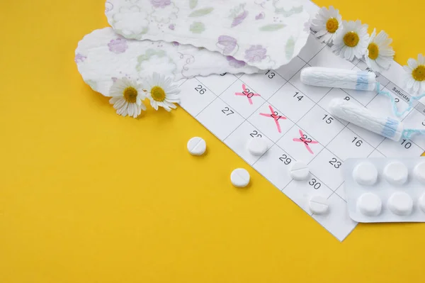 黄色の背景にカモミールと月経期間カレンダー上の月経パッドやタンポン 女性の健康 重要な日の間の個人的な衛生の概念 — ストック写真