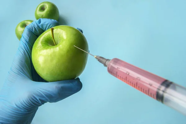 Green apple and syringe with GMO in hands on a blue background. GMO concept with vegetables and fruits.